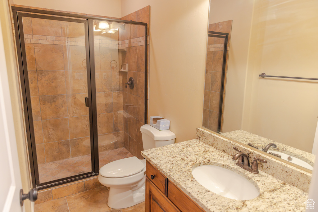 Bathroom with a shower with shower door, toilet, vanity with extensive cabinet space, and tile flooring