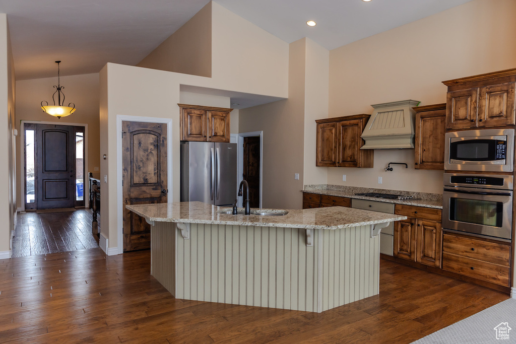 Kitchen featuring dark hardwood / wood-style flooring, a kitchen breakfast bar, custom range hood, stainless steel appliances, and a kitchen island with sink
