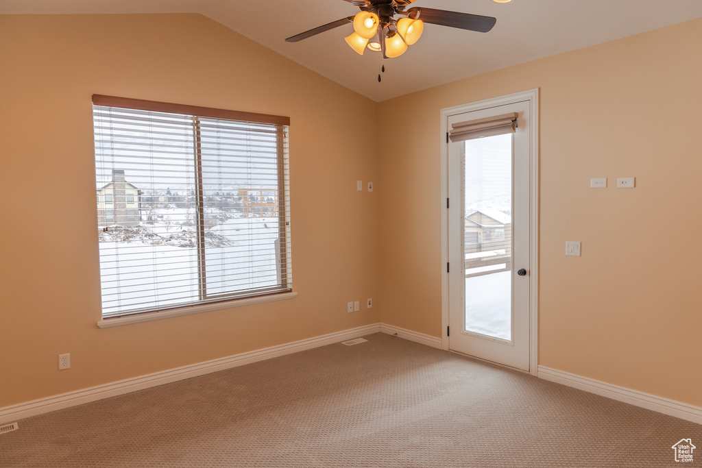 Empty room featuring light carpet, a healthy amount of sunlight, vaulted ceiling, and ceiling fan