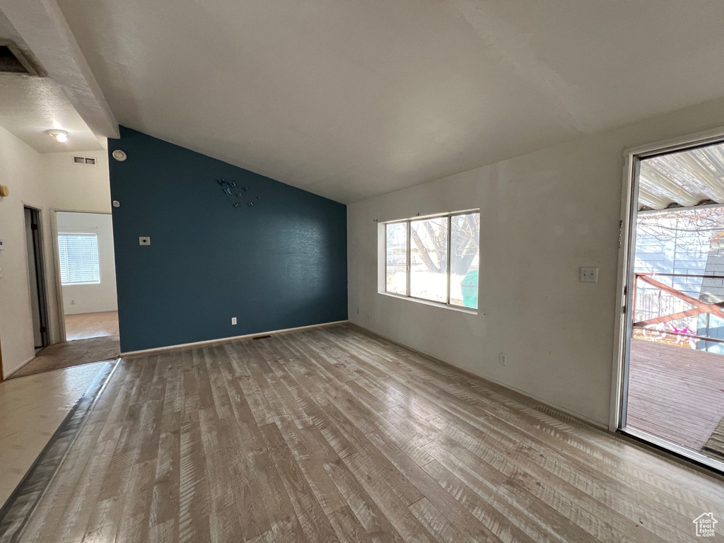 Empty room with vaulted ceiling and light hardwood / wood-style floors