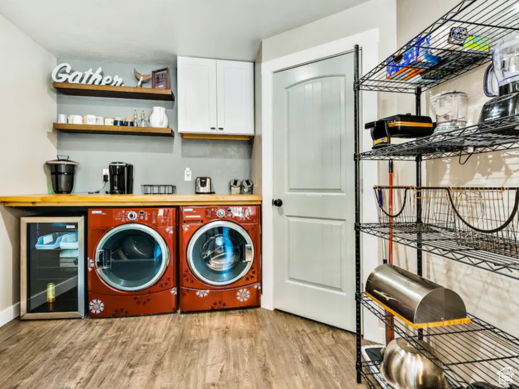 Clothes washing area featuring washing machine and clothes dryer, light hardwood / wood-style floors, bar area, and beverage cooler