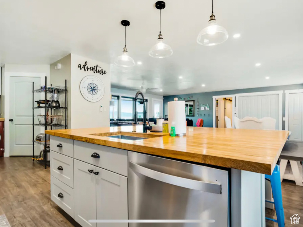 Kitchen featuring stainless steel dishwasher, hanging light fixtures, butcher block countertops, dark hardwood / wood-style floors, and white cabinets