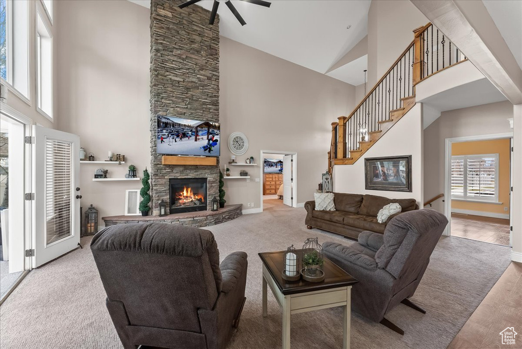 Living room with a stone fireplace, light carpet, high vaulted ceiling, and ceiling fan