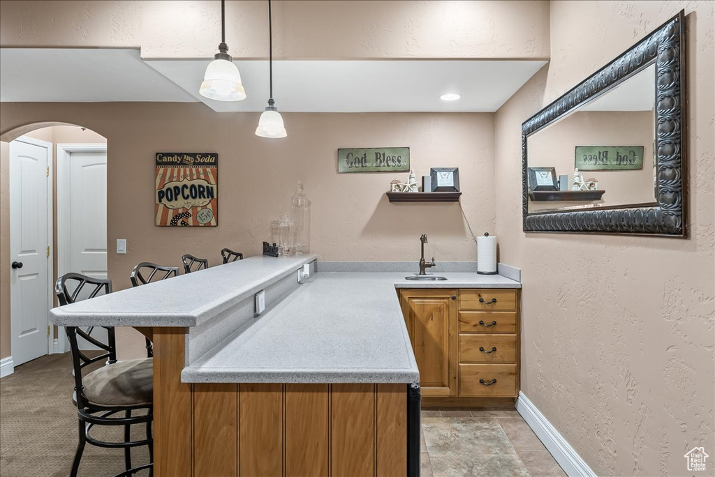 Kitchen featuring kitchen peninsula, a kitchen breakfast bar, decorative light fixtures, light carpet, and sink