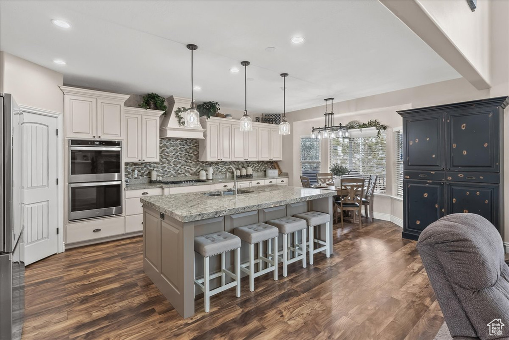 Kitchen with dark hardwood / wood-style flooring, tasteful backsplash, light stone countertops, a kitchen bar, and a chandelier