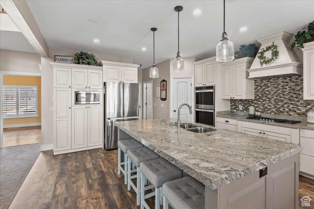 Kitchen with custom exhaust hood, stainless steel appliances, hanging light fixtures, and backsplash