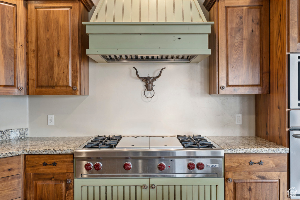 Kitchen featuring gas stove, oven, premium range hood, and light stone counters