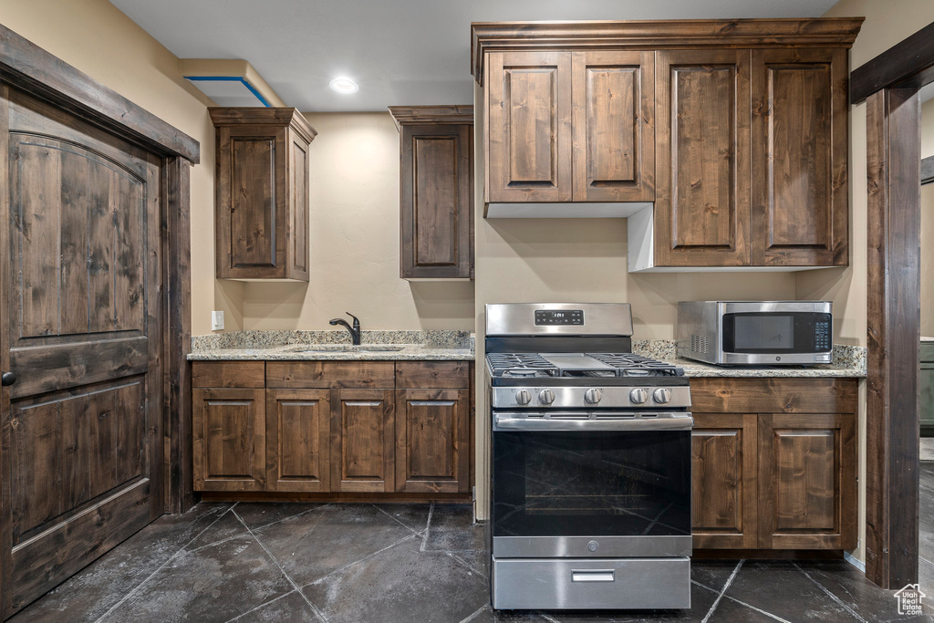 Kitchen featuring dark tile flooring, dark brown cabinetry, appliances with stainless steel finishes, and light stone countertops