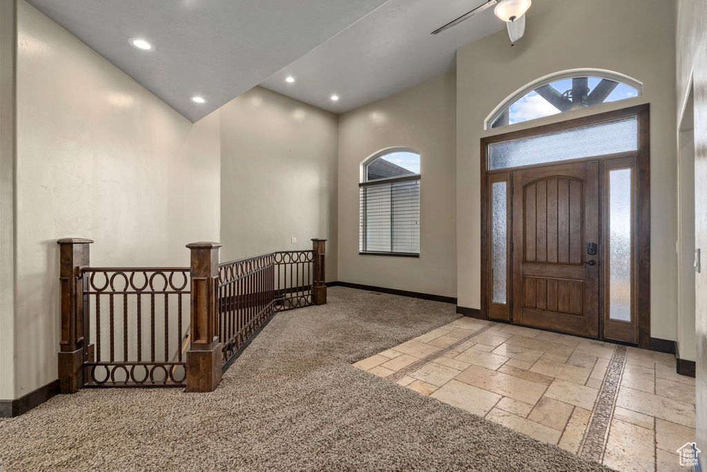 Foyer entrance featuring light colored carpet, high vaulted ceiling, and ceiling fan