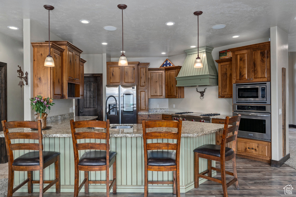 Kitchen featuring a kitchen breakfast bar, premium range hood, light stone countertops, dark wood-type flooring, and stainless steel appliances