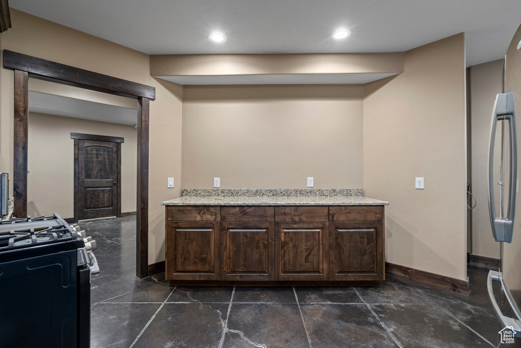 Kitchen featuring dark brown cabinetry, gas range, stainless steel refrigerator, and dark tile floors