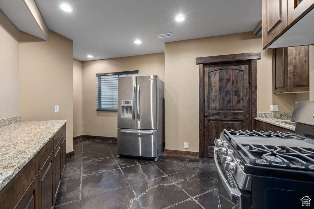 Kitchen with dark brown cabinetry, light stone counters, dark tile floors, range with gas stovetop, and stainless steel refrigerator with ice dispenser