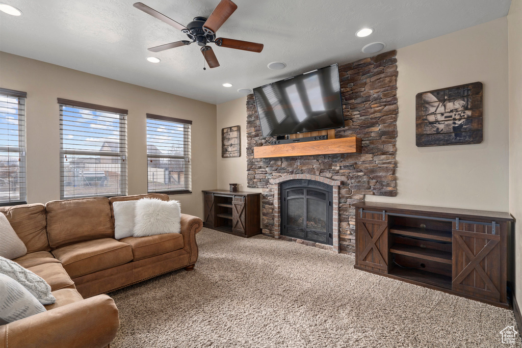 Carpeted living room with a stone fireplace and ceiling fan