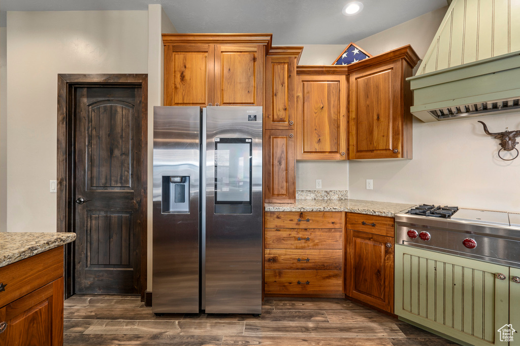 Kitchen with dark wood-type flooring, light stone countertops, stainless steel appliances, and custom range hood