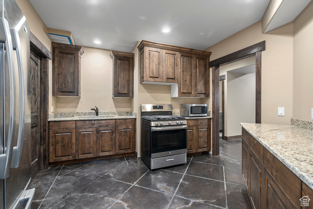 Kitchen with dark brown cabinetry, light stone counters, dark tile floors, appliances with stainless steel finishes, and sink