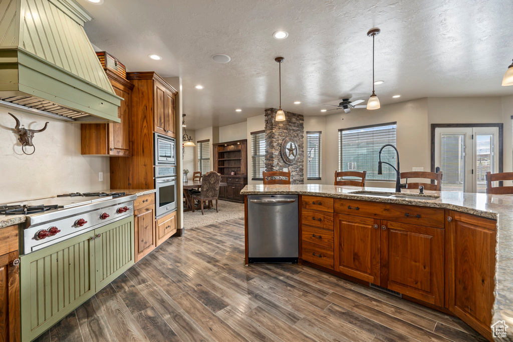 Kitchen with dark wood-type flooring, hanging light fixtures, appliances with stainless steel finishes, and custom range hood