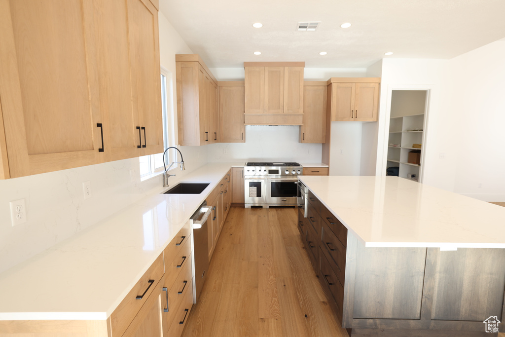 Kitchen featuring light brown cabinetry, stainless steel appliances, custom exhaust hood, light wood-style floors, and a center island