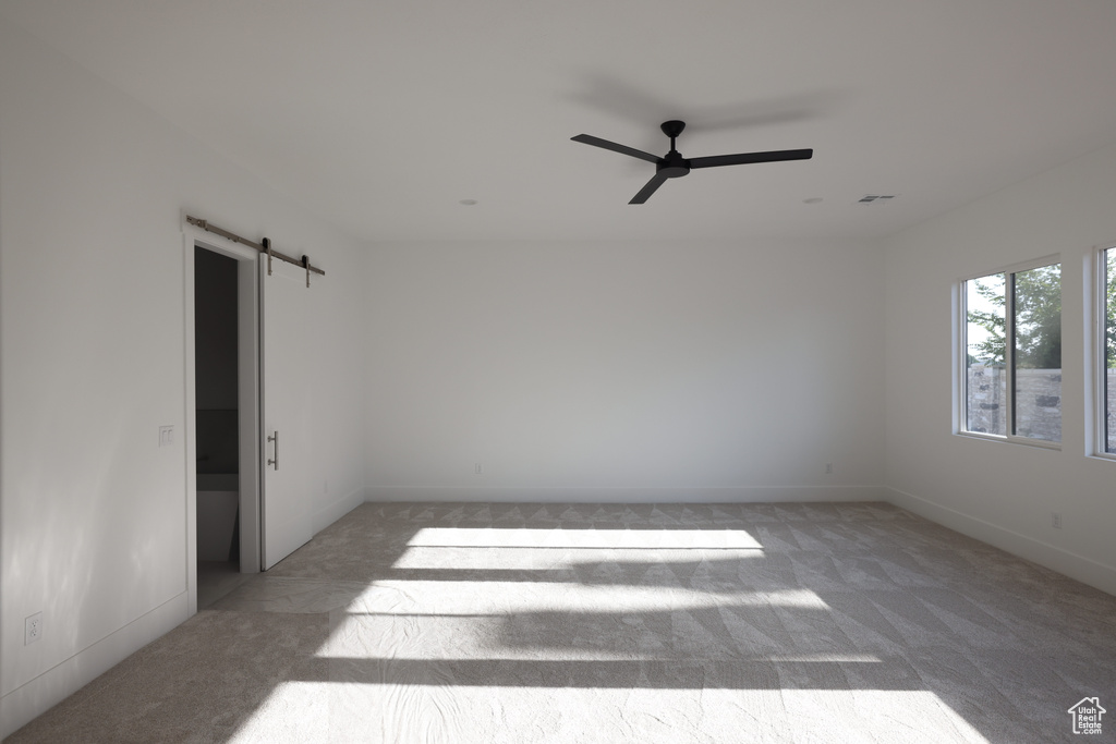 Empty room with a barn door, carpet floors, and ceiling fan