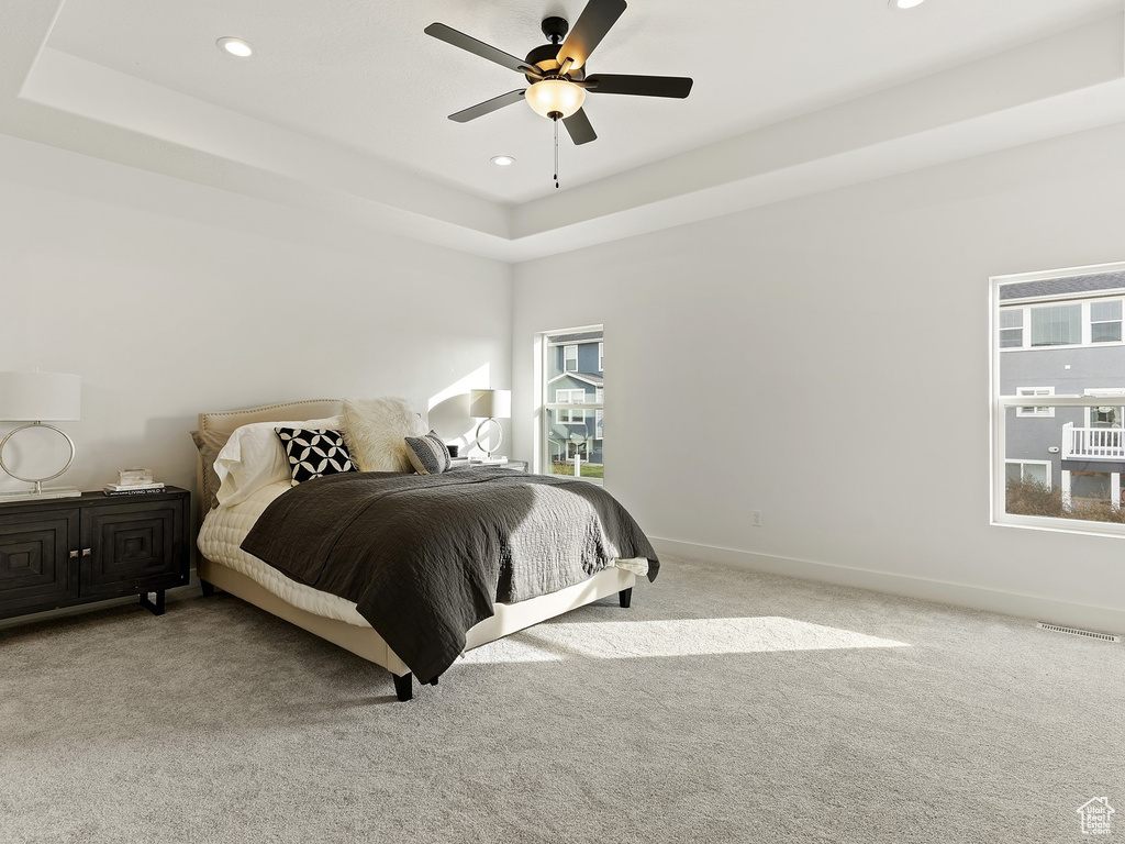 Carpeted bedroom featuring multiple windows, a raised ceiling, and ceiling fan