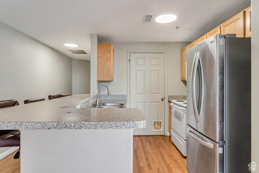 Kitchen with light wood-type flooring, stainless steel refrigerator, white electric range oven, a kitchen breakfast bar, and sink
