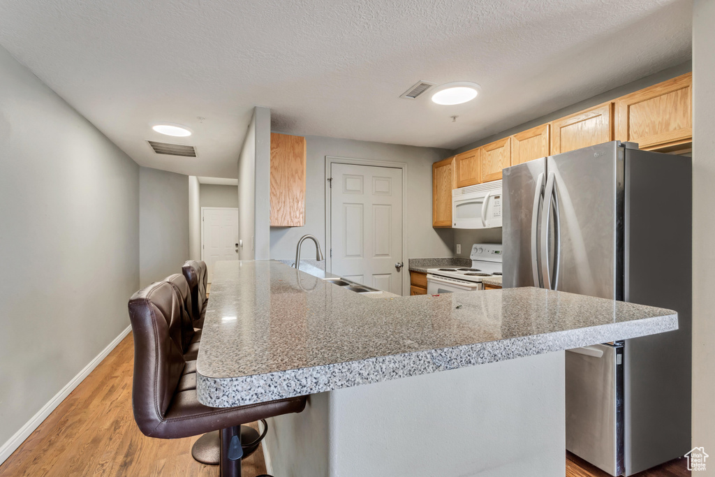 Kitchen with light hardwood / wood-style floors, a kitchen breakfast bar, sink, white appliances, and kitchen peninsula