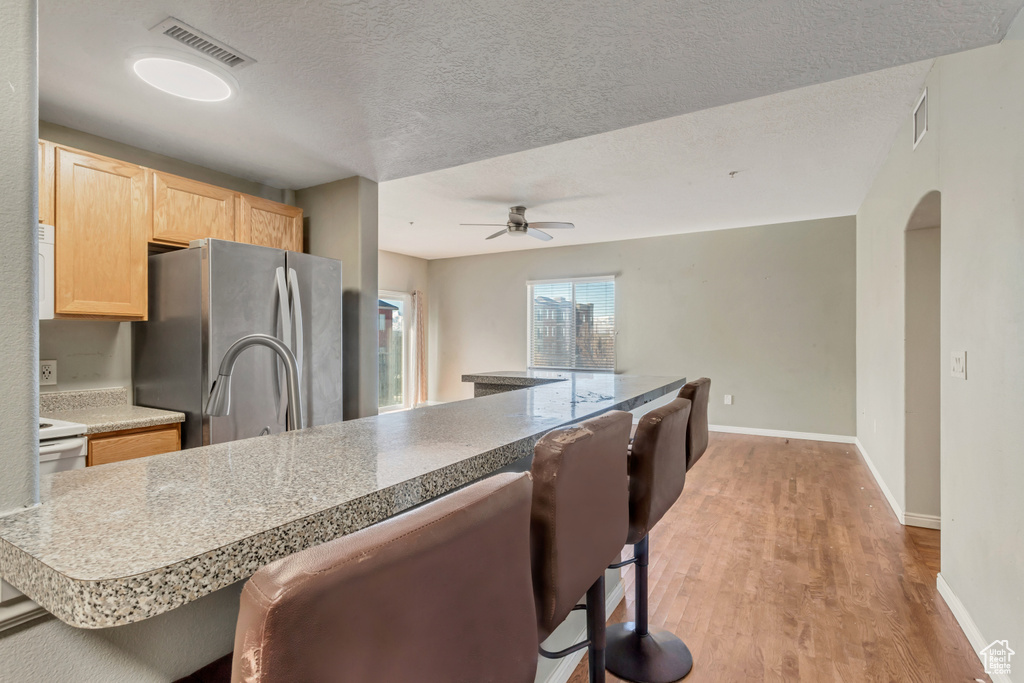 Kitchen featuring light hardwood / wood-style flooring, a textured ceiling, ceiling fan, stainless steel fridge, and a breakfast bar
