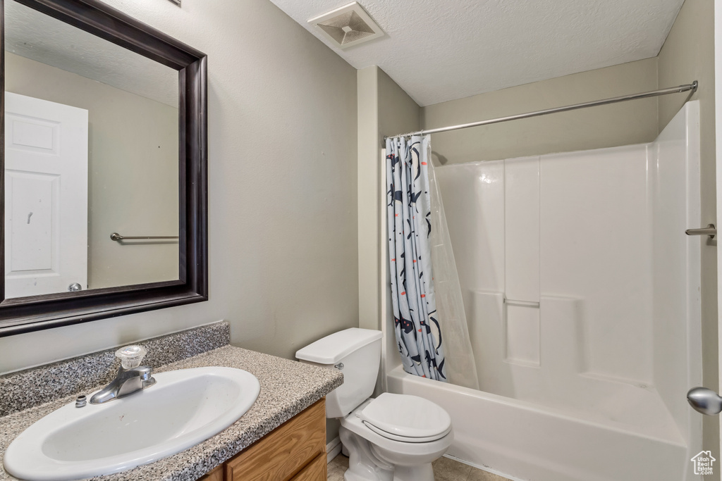 Full bathroom featuring toilet, shower / tub combo, a textured ceiling, and vanity with extensive cabinet space