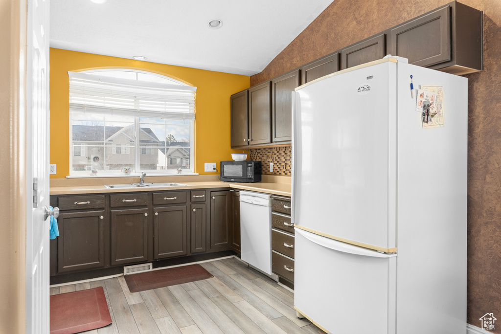 Kitchen with lofted ceiling, white appliances, backsplash, light hardwood / wood-style flooring, and sink