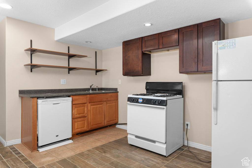 Kitchen with dark brown cabinetry, sink, white appliances, and tile flooring