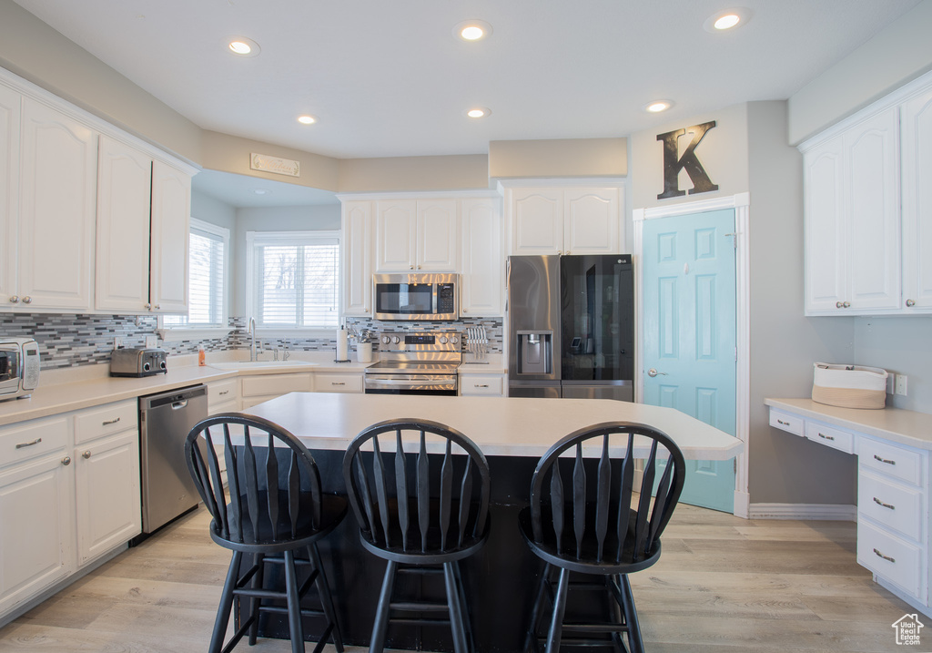 Kitchen featuring tasteful backsplash, stainless steel appliances, white cabinets, and light hardwood / wood-style flooring