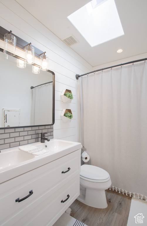 Bathroom with vanity, a skylight, hardwood / wood-style flooring, toilet, and backsplash