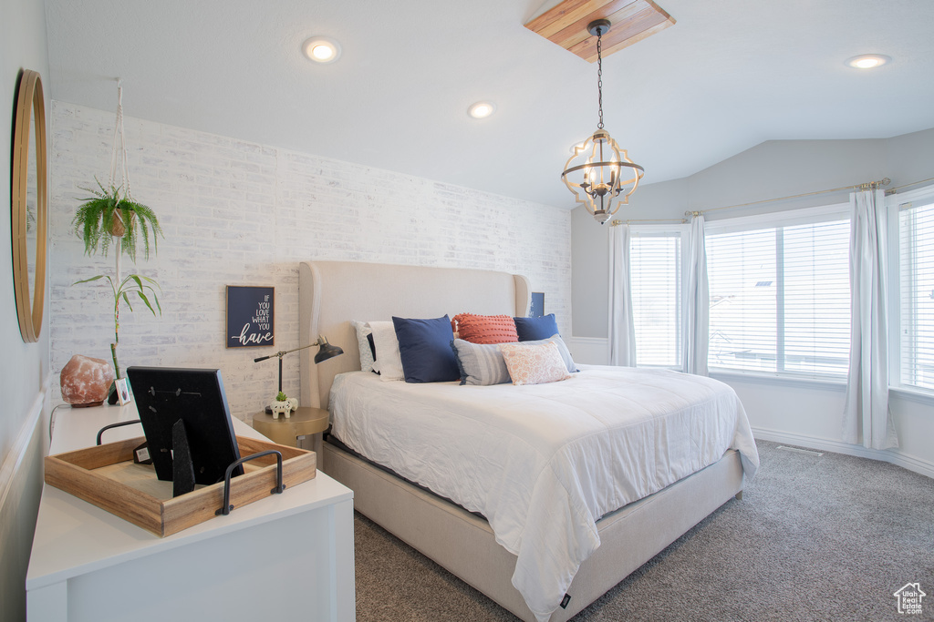 Bedroom featuring lofted ceiling, a notable chandelier, brick wall, and carpet flooring