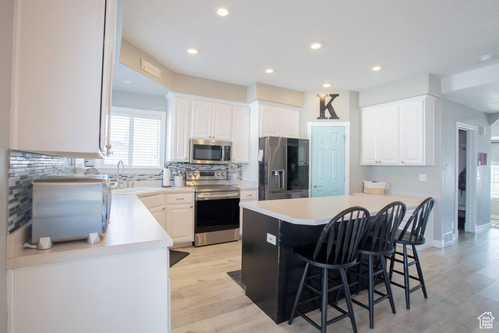 Kitchen with white cabinets, a breakfast bar area, light hardwood / wood-style floors, and appliances with stainless steel finishes