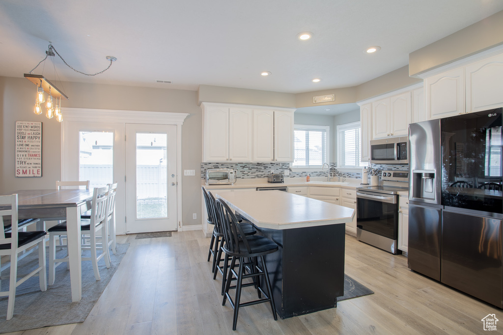 Kitchen with a breakfast bar, white cabinets, appliances with stainless steel finishes, light hardwood / wood-style flooring, and tasteful backsplash