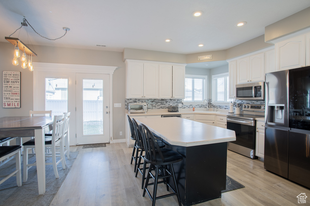 Kitchen featuring a kitchen breakfast bar, white cabinets, appliances with stainless steel finishes, light hardwood / wood-style flooring, and backsplash