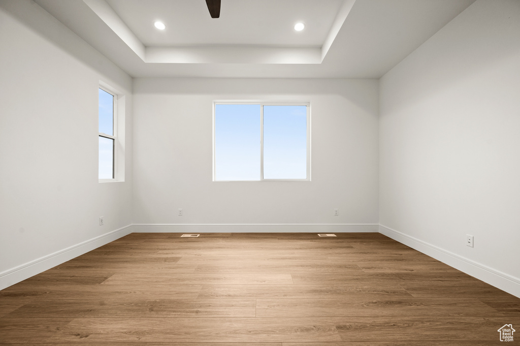 Empty room with light wood-type flooring, a raised ceiling, and ceiling fan