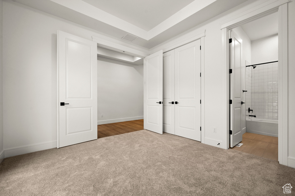 Unfurnished bedroom with ensuite bathroom, a closet, and light colored carpet