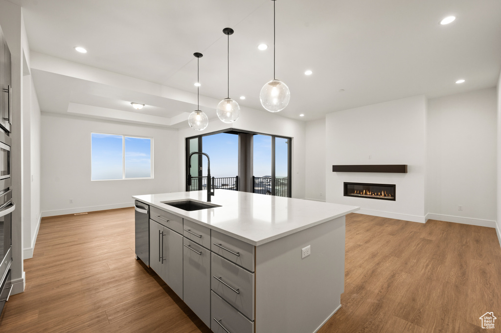 Kitchen with a healthy amount of sunlight, sink, light wood-type flooring, gray cabinetry, and a center island with sink