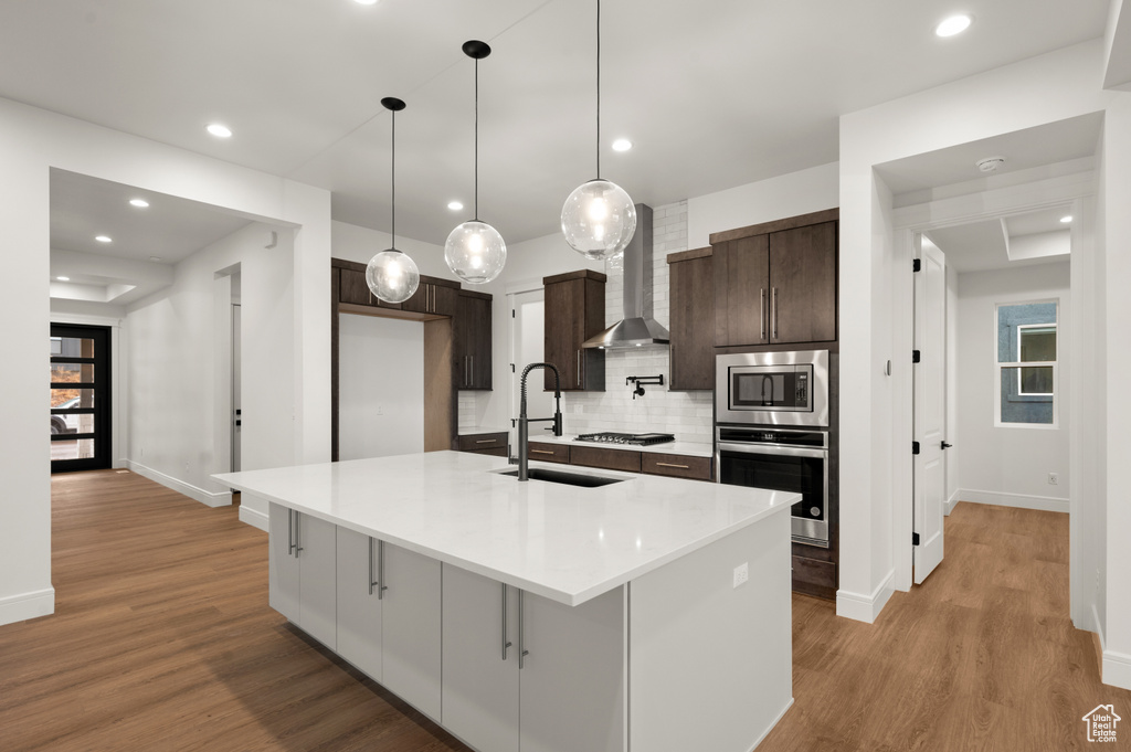 Kitchen featuring light hardwood / wood-style floors, appliances with stainless steel finishes, an island with sink, and backsplash