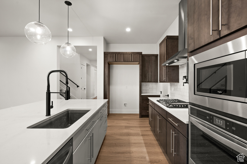 Kitchen featuring light hardwood / wood-style floors, tasteful backsplash, wall chimney exhaust hood, sink, and stainless steel appliances