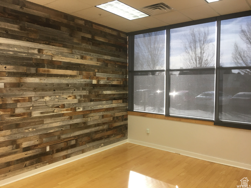 Empty room featuring wood walls, a drop ceiling, and hardwood / wood-style flooring