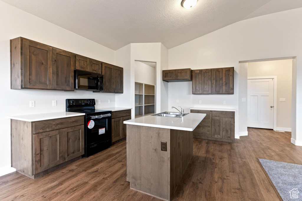 Kitchen featuring dark hardwood / wood-style flooring, black appliances, an island with sink, lofted ceiling, and sink