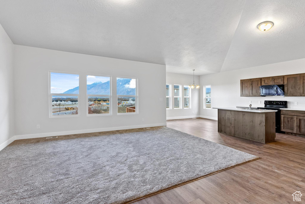 Interior space with pendant lighting, carpet flooring, a kitchen island with sink, a notable chandelier, and vaulted ceiling