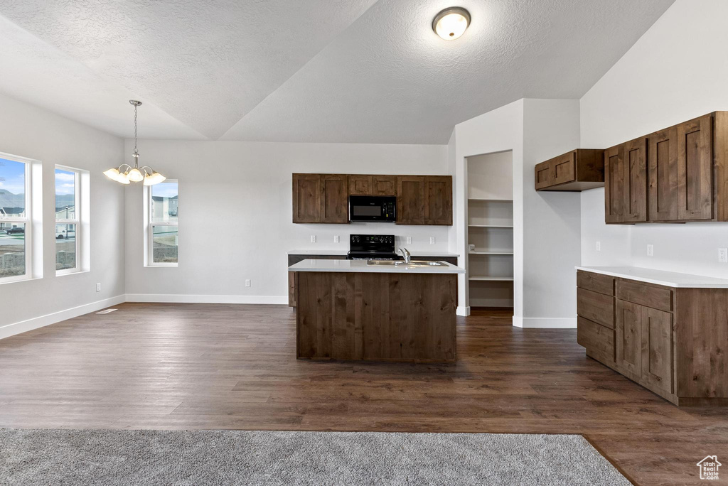 Kitchen with pendant lighting, dark wood-type flooring, a kitchen island with sink, a notable chandelier, and stove