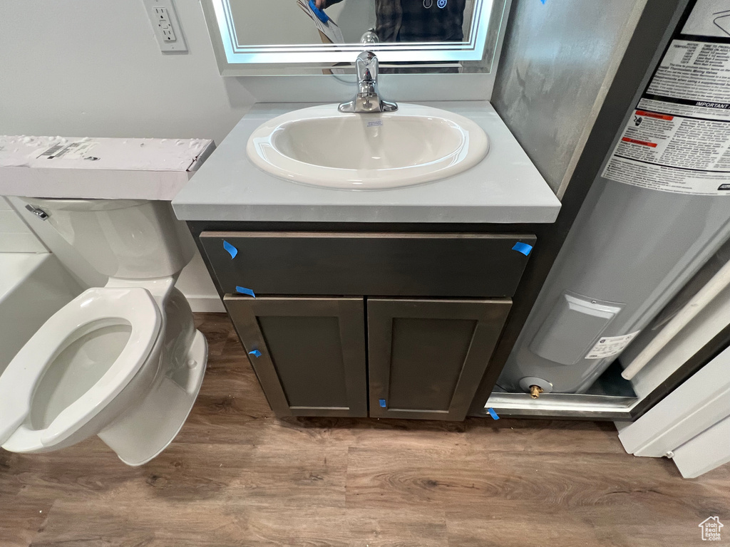 Bathroom featuring electric water heater, vanity, toilet, and hardwood / wood-style floors