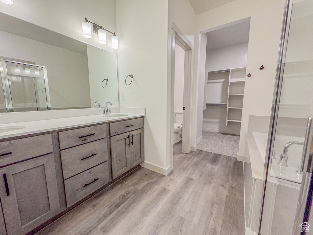 Bathroom with hardwood / wood-style floors, a bath to relax in, vanity with extensive cabinet space, dual sinks, and toilet