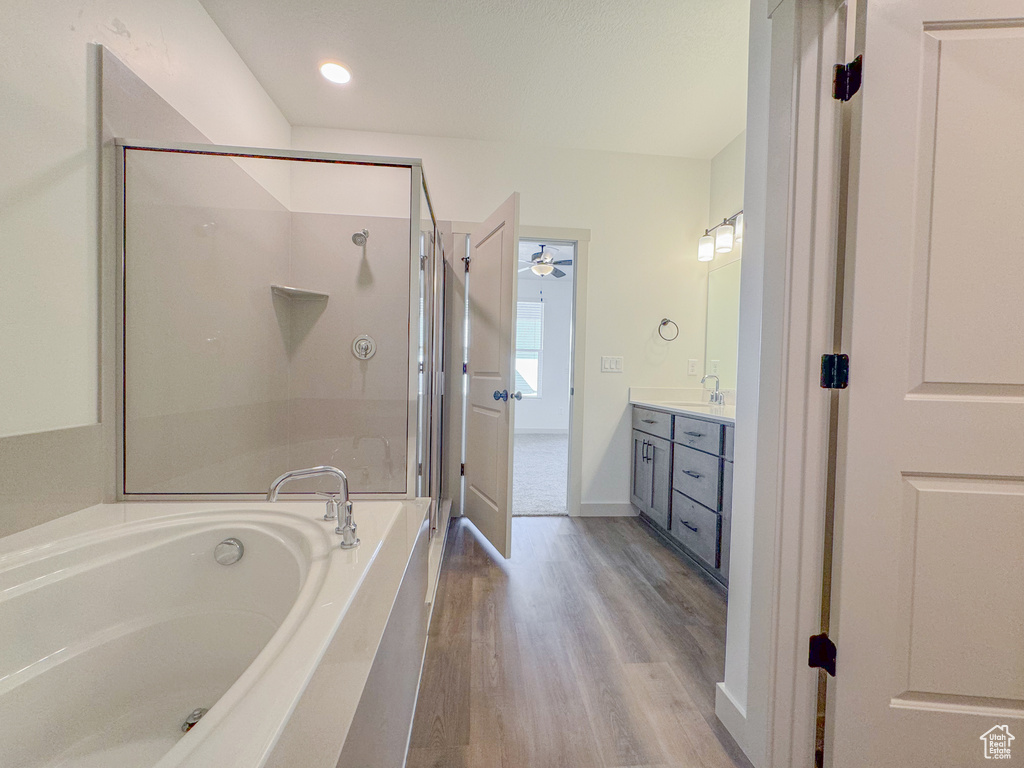 Bathroom featuring hardwood / wood-style flooring, ceiling fan, vanity, and plus walk in shower