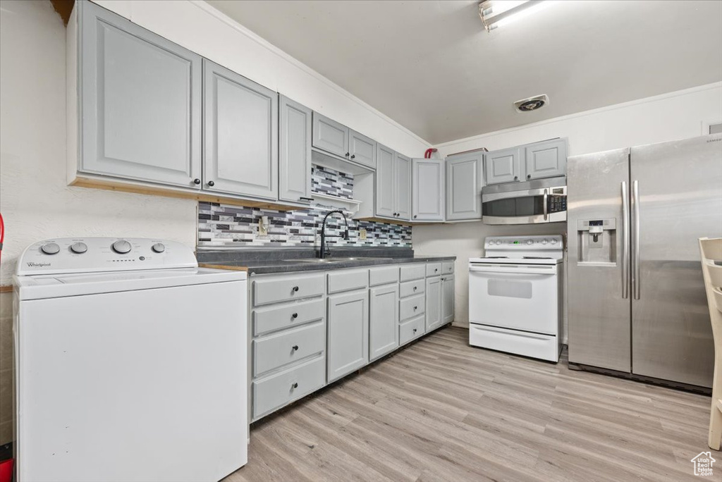 Kitchen with appliances with stainless steel finishes, light hardwood / wood-style flooring, sink, washer / dryer, and gray cabinetry