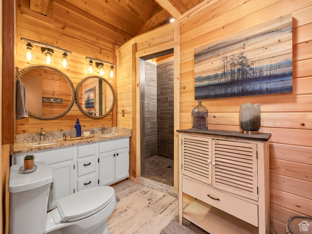 Bathroom featuring a tile shower, wooden ceiling, toilet, vanity with extensive cabinet space, and wood walls