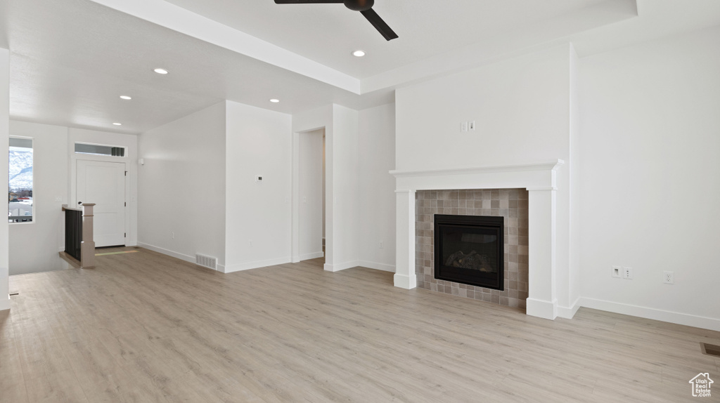 Unfurnished living room with a tiled fireplace, a tray ceiling, light hardwood / wood-style flooring, and ceiling fan